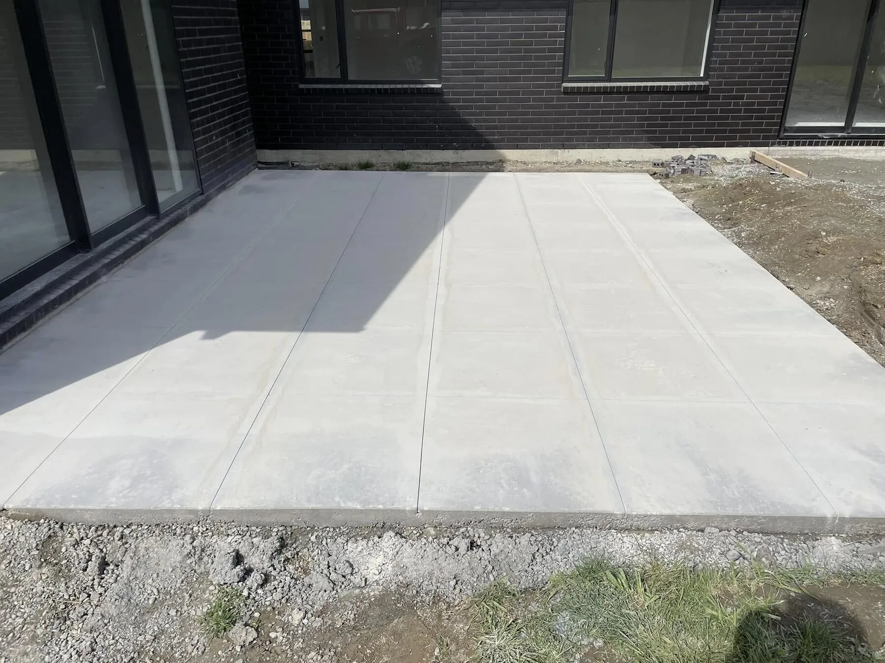 Concrete patio wrapping the corner of a dark brick house in South Canterbury, decorative cuts carried around the return