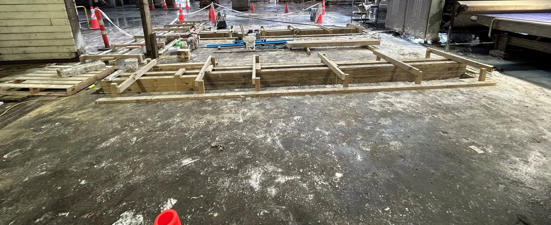 Boxed slot drains cut into a live factory floor in Timaru, with cones and barrier tape across the working area behind