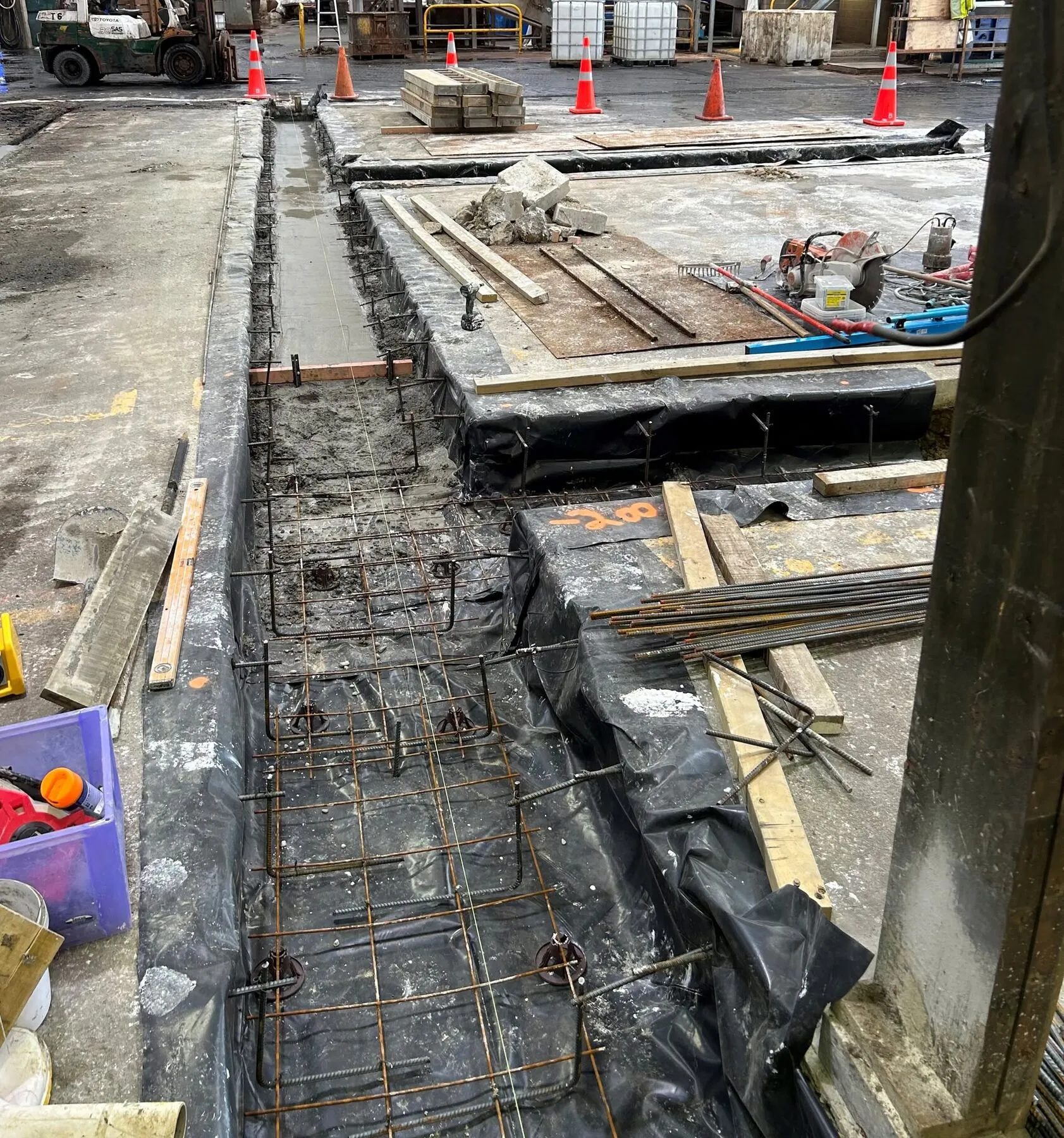 Reinforcing steel and polythene laid in an open drainage trench on a Timaru factory floor