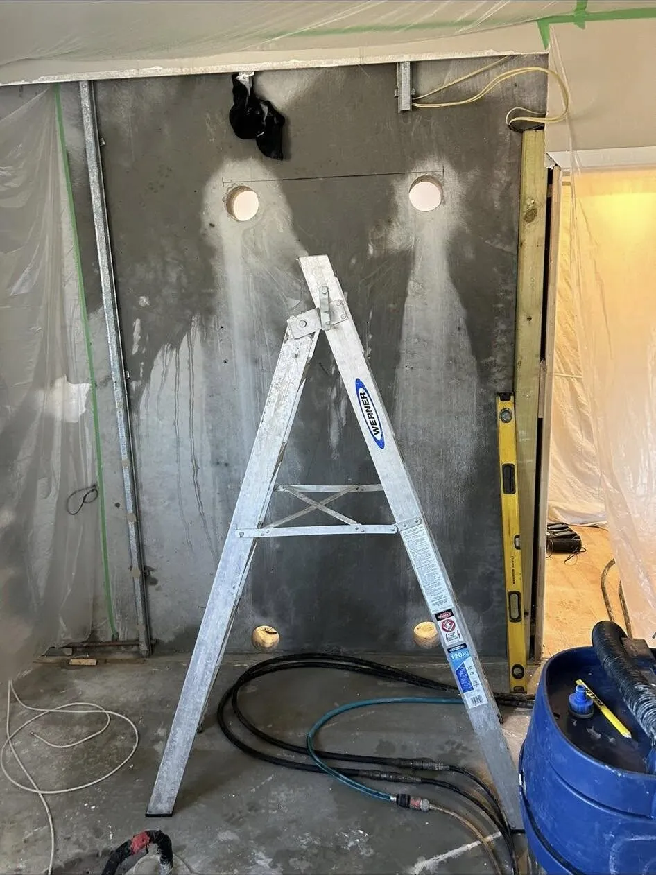 Interior concrete wall in South Canterbury part cut for a doorway, with plastic sheeting, work lights, vacuum and hoses set up around it